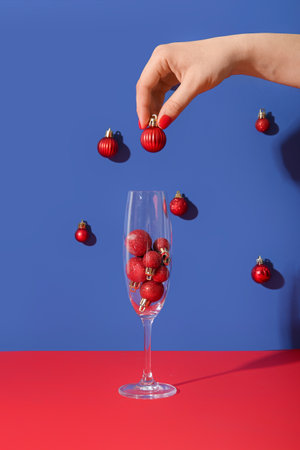 Female hand with red manicure, champagne glass and Christmas baubles on blue backgroundの写真素材