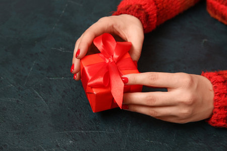 Female hands with red manicure and Christmas gift box on black grunge backgroundの写真素材