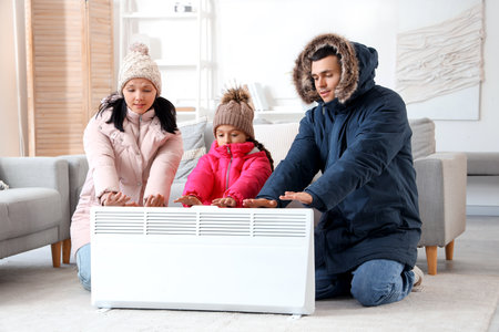Frozen family in winter clothes warming near radiator at homeの写真素材