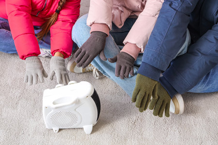 Frozen family in winter clothes warming near electric heater at home, closeupの写真素材