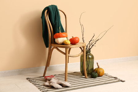 Chair with pumpkins and tree branches in vase near beige wallの写真素材