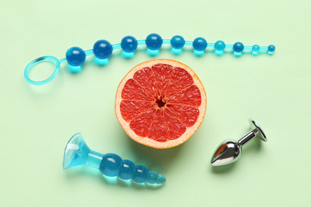 Different anal plugs from sex shop and half of tasty grapefruit on green backgroundの写真素材