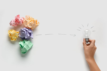 Female hand with crumpled paper and light bulb on white background. Business idea concept