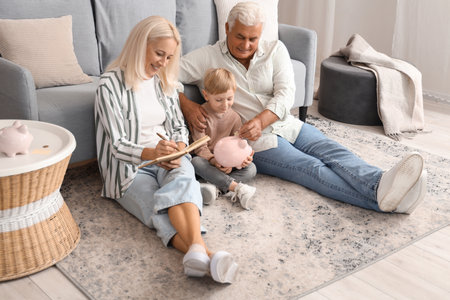 Little boy with his grandparents putting coin in piggy bank at homeの写真素材