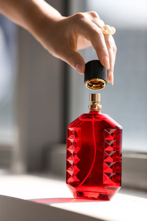 Female hand with bottle of elegant perfume on windowsill at homeの写真素材