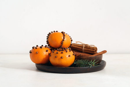 Wooden plate with pomander balls and cinnamon on white background