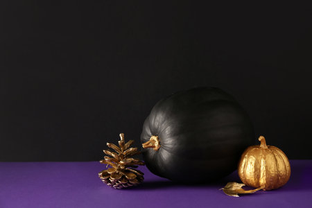 Painted pumpkins with golden cone and leaf on purple table near black wallの写真素材
