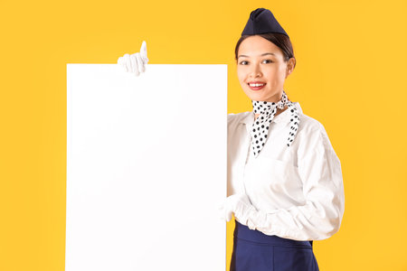 Beautiful Asian stewardess with blank poster on yellow backgroundの写真素材