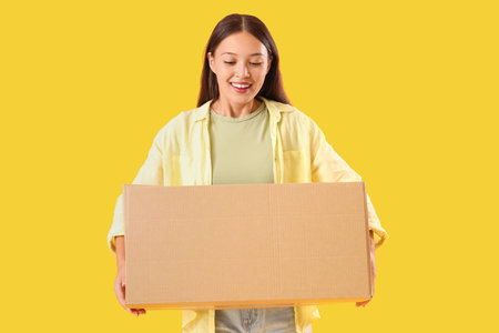 Young Asian woman with parcel on yellow background