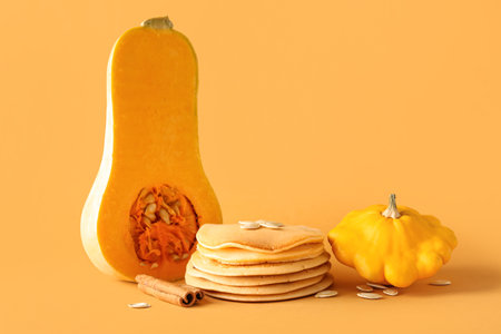 Tasty pumpkin pancakes with seeds and cinnamon on orange backgroundの写真素材