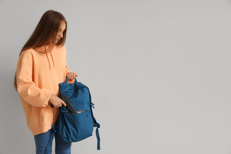 Female student with gun and backpack near light wall. School shooting concept