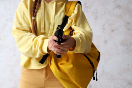Female student with gun near grunge wall, closeup. School shooting concept