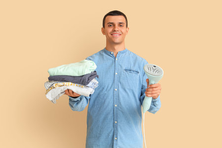 Young man with steamer and clothes on beige backgroundの写真素材