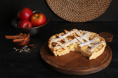 Wooden board of delicious apple pie with almond and cinnamon on black backgroundの写真素材