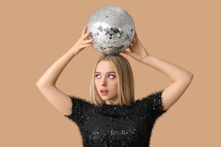 Beautiful thoughtful young woman with disco ball on brown backgroundの写真素材