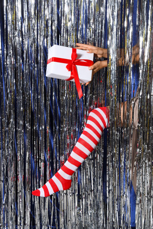 Woman in Christmas stockings with Christmas gift against silver tinselの写真素材