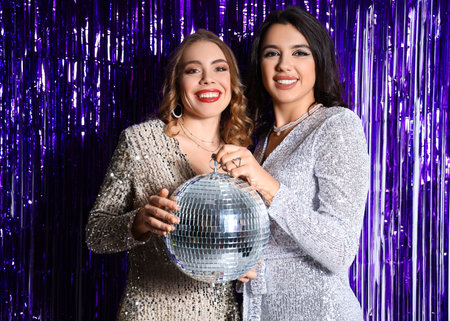 Beautiful young women with disco ball against violet tinsel