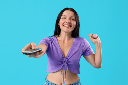 Joyful young woman with remote control watching TV on blue background