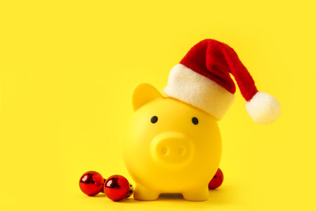 Piggy bank with Santa hat and Christmas balls on yellow backgroundの写真素材