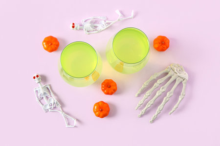 Skeletons with pumpkins and glasses of tasty cocktail for Halloween celebration on pink backgroundの写真素材