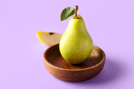 Bowl with ripe pear on lilac background
