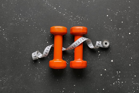 Dumbbells and measuring tape on black backgroundの写真素材