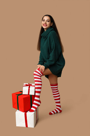 Beautiful young woman in Christmas stockings with gift boxes on brown backgroundの写真素材