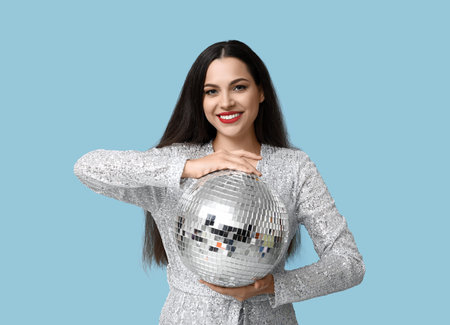 Beautiful young woman with disco ball on blue background