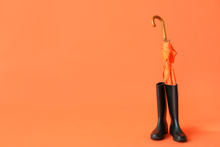 Orange stylish umbrella and black gumboots on color backgroundの写真素材