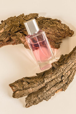 Pink bottle of perfume and tree bark on white background