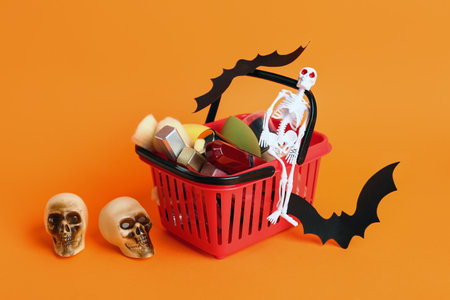 Shopping basket with lipsticks, different decorative cosmetics and Halloween decor on orange backgroundの写真素材
