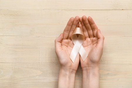 Woman with beige ribbon on light wooden background. Uterine cancer awareness conceptの写真素材
