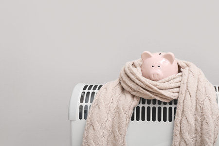 Piggy bank with scarf on radiator near light wall. Winter heating conceptの写真素材