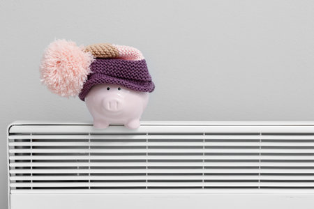 Piggy bank with hat on radiator near light wall. Winter heating conceptの写真素材