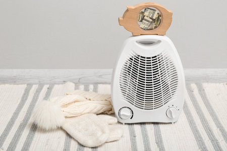 Piggy bank with money on electric fan heater near light wallの写真素材