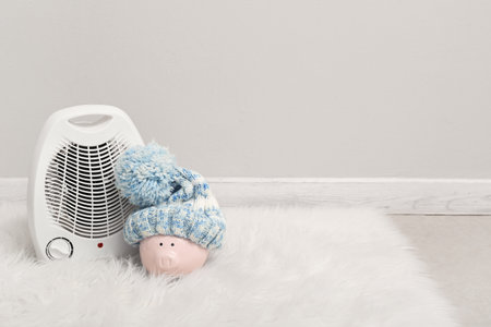 Piggy bank with hat and electric fan heater near light wallの写真素材