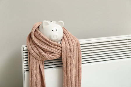Piggy bank with scarf on radiator near light wall. Winter heating conceptの写真素材
