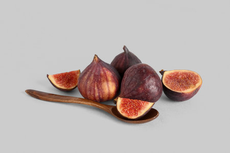 Fresh ripe figs and wooden spoon with piece on white background