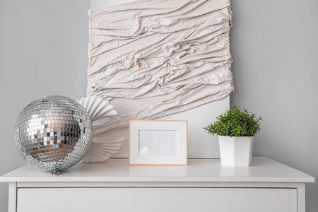 Chest of drawers with disco ball, blank frame and houseplant in modern living room