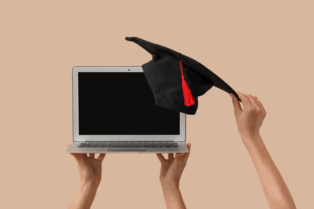 Women with blank laptop and graduation hat on beige backgroundの写真素材