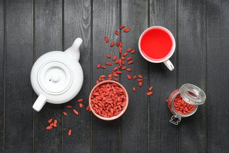 Bowl with red dried goji berries and cup of hot tea on black wooden backgroundの写真素材