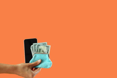 Woman with blank mobile phone and money on orange background