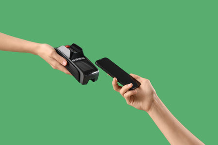 Woman with mobile phone paying via terminal on green background