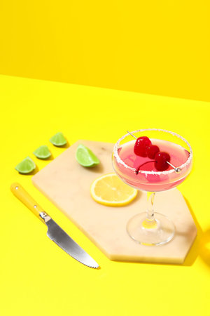 Glass of Cosmopolitan cocktail with cherries and lemon on yellow backgroundの写真素材