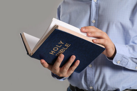 Young man reading Bible on gray background, closeup