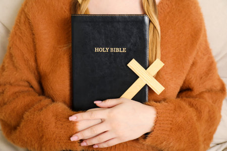 Young woman with wooden cross and Bible in living room, closeupの写真素材