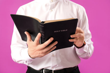 Young man reading Bible on purple background, closeupの写真素材