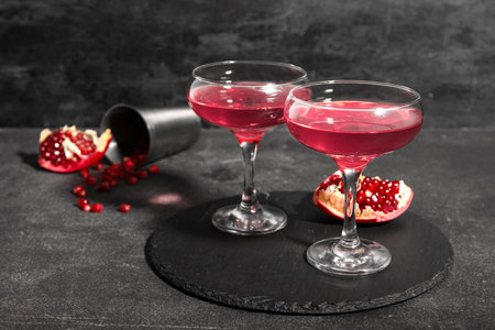 Board with glasses of Cosmopolitan cocktail and pomegranate on black backgroundの写真素材