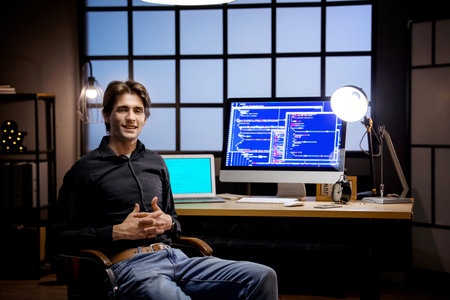 Happy young male programmer working with computers in office at night