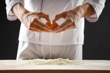 Young chef preparing dough for bread on table against black backgroundの写真素材